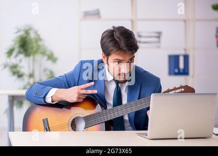 Jeune homme d'affaires jouant de la guitare sur le lieu de travail Banque D'Images