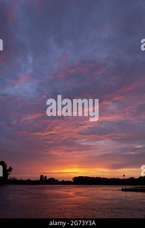 Cadre vertical de réflexion dans la rivière IJssel avec des arbres silhouettés d'un spectaculaire ciel de coucher de soleil intense et coloré avec texture et détail des nuages Banque D'Images