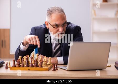 Un vieux employé d'homme d'affaires jouant aux échecs sur le lieu de travail Banque D'Images