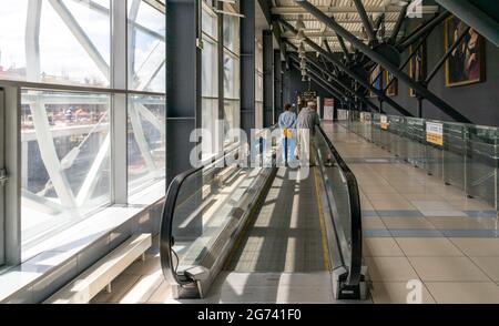 Couple âgé, homme avec un bâton de marche et femme sur un passage en mouvement dans l'aéroport, vue arrière, Tolmachevo, Novosibirsk, Russie Banque D'Images