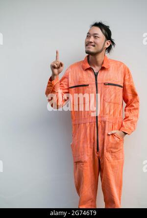 Le mécanicien en chef dans un uniforme orange pointant un doigt vers le haut. Portrait sur fond gris avec lumière studio. Banque D'Images