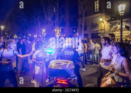 Barcelone, Espagne. 10 juillet 2021. Un policier sur une moto vu passer par une foule de personnes avec des boissons alcoolisées dans la rue. Le gouvernement de Catalogne a annoncé le dernier jour de juillet 6 la fermeture de la vie nocturne dans les espaces intérieurs, une mesure qui a commencé ce week-end, en raison de la menace de la cinquième vague de Covid-19. Dans les rues de Barcelone, la police a expulsé les gens qui boivent dans les foules. Crédit : SOPA Images Limited/Alamy Live News Banque D'Images