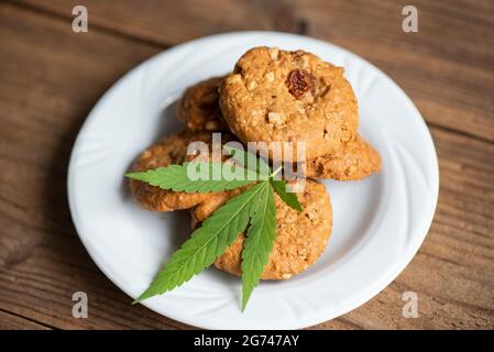 Biscuits au chocolat avec feuille de cannabis - la marijuana feuilles plante sur plaque blanche sur la table en bois nature herbe, cannabis concept alimentaire Banque D'Images