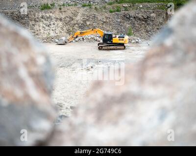 Pelle hydraulique lourde travaillant sur le terrassement dans une mine de granit ouverte. La machine à chenilles effectue des travaux d'excavation en carrière Banque D'Images