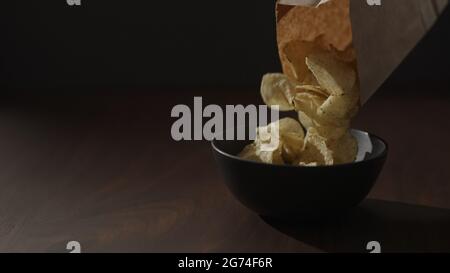 croustilles biologiques dans un bol noir sur une table en noyer, photo large Banque D'Images