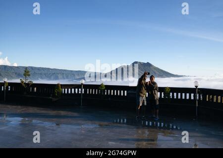 BALI, INDONÉSIE-FÉV 23 2019 : deux touristes, locaux et étrangers, prenant une photo ensemble sur fond de Mont Batur Bali couvert de nuage stratus Banque D'Images