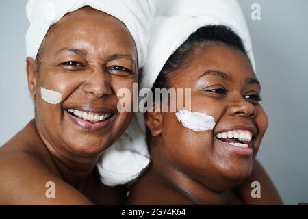 Mère africaine et fille faisant des soins de beauté à la maison en utilisant le masque de peau - soins du corps et concept de famille - Focus sur la bouche de fille Banque D'Images