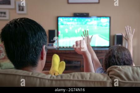 Les gens regardent le sport en streaming à la télévision, applaudissent avec la poing et les mains levées. Restez à la maison. Banque D'Images