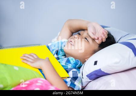 Un enfant fatigué et ennuyé malheureux lorsqu'il a lu un livre sur le lit dans la chambre. Les enfants lisent et étudient, étudiant dur, étudiant fatigué, concept d'éducation. Banque D'Images