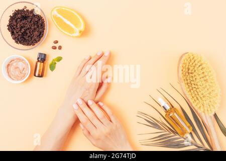 Les mains de la femme appliquent de l'argile organique à côté des cosmétiques naturels anti-cellulite à l'huile de café et brosse en bois pour le massage sec sur fond beige Banque D'Images