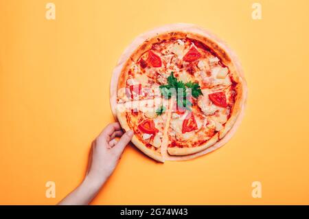 Une femme prend une tranche de pizza, sur un fond orange sans couture. Vue de dessus Banque D'Images