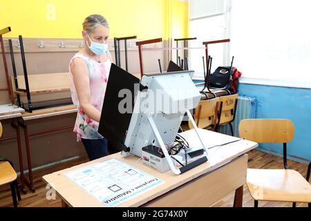 Les personnes ayant un masque utilisent un système de vote lors des élections législatives bulgares à Sofia, en Bulgarie, le 11 juillet 2021 Banque D'Images