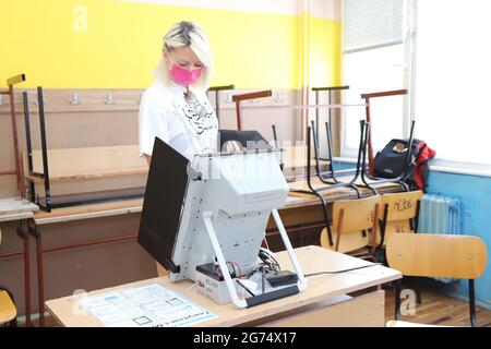 Les personnes ayant un masque utilisent un système de vote lors des élections législatives bulgares à Sofia, en Bulgarie, le 11 juillet 2021 Banque D'Images