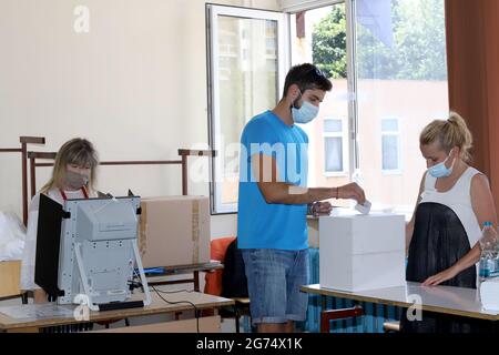 Les personnes ayant un masque utilisent un système de vote lors des élections législatives bulgares à Sofia, en Bulgarie, le 11 juillet 2021 Banque D'Images