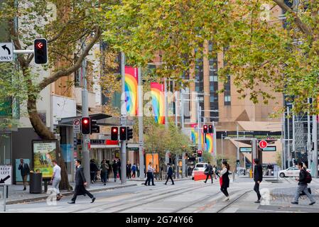 La plupart du temps dépourvus de voitures et d'autobus, les piétons traversent les lignes de tramway de George Street et les drapeaux arc-en-ciel volent depuis les poteaux de Sydney, Nouvelle-Galles du Sud. Banque D'Images