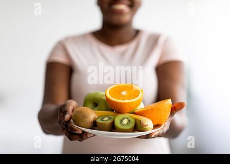 Un régime alimentaire minceur, une perte de poids et un mode de vie sain. Vue rognée d'une femme noire de taille plus tenant une assiette de fruits à l'intérieur Banque D'Images