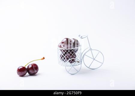 Cerise dans un vélo miniature. Vélo jouet avec baies sur fond blanc. Gros plan, espace de copie pour le texte. Banque D'Images