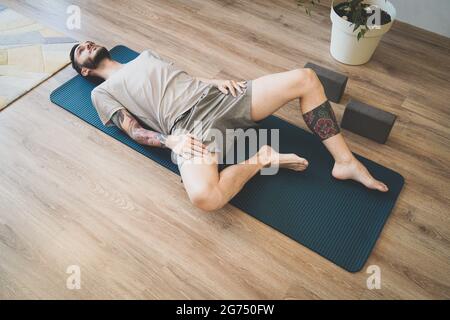 Vue de dessus de l'homme tatoué méditant sur le tapis de sport à la maison Banque D'Images