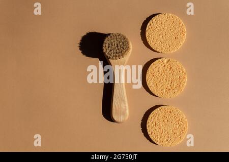 Accessoires de douche - brosse pour le visage avec soies naturelles et éponges rondes en cellulose sur fond marron, vue du dessus. Nettoyage du concept de santé de la peau Banque D'Images