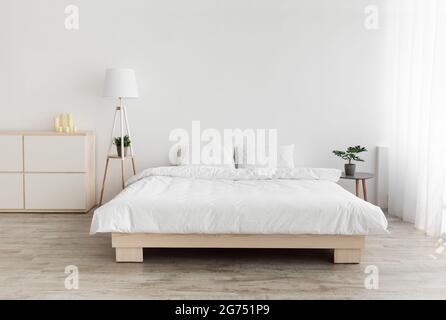 Véritable photo de l'intérieur de la chambre dans un style simple. Grand lit avec oreillers, lampe et mobilier, mur blanc, espace vide Banque D'Images