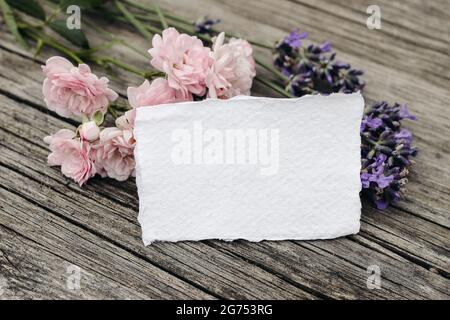 Papeterie florale scène de vie. Maquette de carte de vœux vierge sur fond de table en bois avec fleurs de lavande et de petites roses roses roses. Vue de dessus Banque D'Images