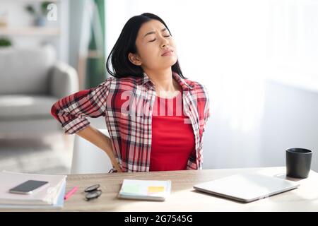 Belle jeune femme asiatique souffrant de mal de dos en travaillant dans le bureau à domicile Banque D'Images