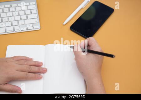 Un coup de tête de mains de femmes écrivant dans un carnet et un clavier sur la table Banque D'Images