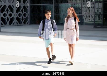 Les enfants, les adolescents, les écoliers, les garçons et les filles, les frères et sœurs de 11 ans sur fond de mur en béton avec des sacs à dos vont à l'école. Banque D'Images