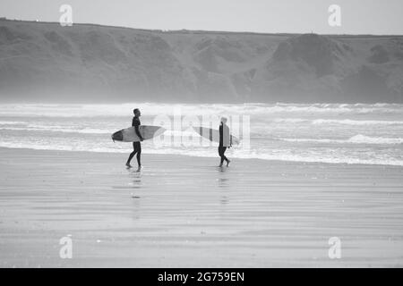 Les surfeurs de tous âges transportent des planches de surf jusqu'au bord de la plage de Llangennith, sur la péninsule de Gower. Image monochrome représentant les activités de plein air Banque D'Images