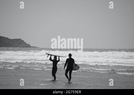 Les surfeurs de tous âges transportent des planches de surf jusqu'au bord de la plage de Llangennith, sur la péninsule de Gower. Image monochrome représentant les activités de plein air Banque D'Images