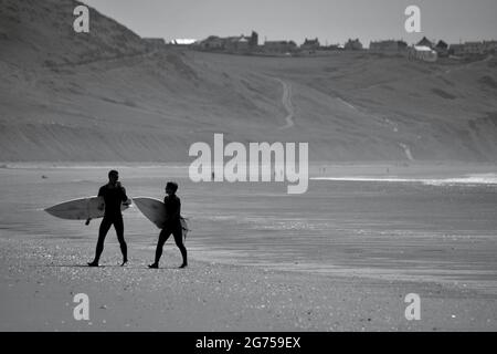 Les surfeurs de tous âges transportent des planches de surf jusqu'au bord de la plage de Llangennith, sur la péninsule de Gower. Image monochrome représentant les activités de plein air Banque D'Images