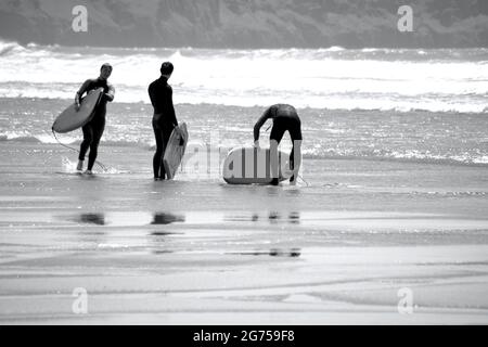 Les surfeurs de tous âges transportent des planches de surf jusqu'au bord de la plage de Llangennith, sur la péninsule de Gower. Image monochrome représentant les activités de plein air Banque D'Images