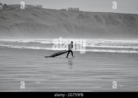 Les surfeurs de tous âges transportent des planches de surf jusqu'au bord de la plage de Llangennith, sur la péninsule de Gower. Image monochrome représentant les activités de plein air Banque D'Images