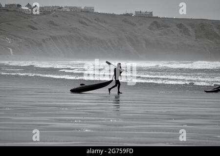 Les surfeurs de tous âges transportent des planches de surf jusqu'au bord de la plage de Llangennith, sur la péninsule de Gower. Image monochrome représentant les activités de plein air Banque D'Images