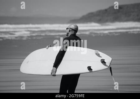 Les surfeurs de tous âges transportent des planches de surf jusqu'au bord de la plage de Llangennith, sur la péninsule de Gower. Image monochrome représentant les activités de plein air Banque D'Images