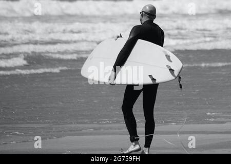 Les surfeurs de tous âges transportent des planches de surf jusqu'au bord de la plage de Llangennith, sur la péninsule de Gower. Image monochrome représentant les activités de plein air Banque D'Images