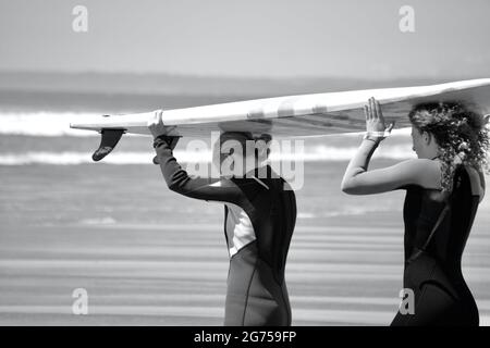 Les surfeurs de tous âges transportent des planches de surf jusqu'au bord de la plage de Llangennith, sur la péninsule de Gower. Image monochrome représentant les activités de plein air Banque D'Images