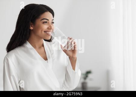 Nutrition utile et équilibre de l'eau pour la peau. Femme afro-américaine millénaire en peignoir d'eau potable, espace vide Banque D'Images