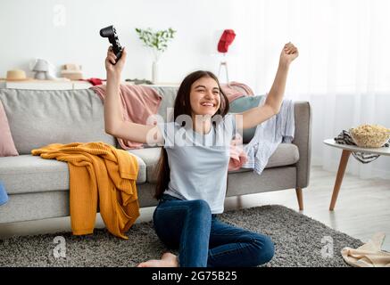 Bonne fille indienne adolescente remportant un jeu vidéo sur PlayStation, s'amuser, célébrer la victoire en intérieur Banque D'Images