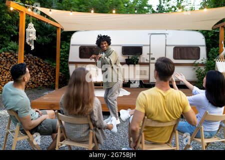 Jeunes amis multiraciaux jouant deviner qui jeu, riant, s'amusant ensemble près de camping-car en plein air Banque D'Images