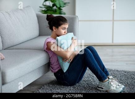 Une adolescente indienne déprimée assise sur le sol à la maison, embrassant l'oreiller, souffrant du manque de communication pendant le covid Banque D'Images