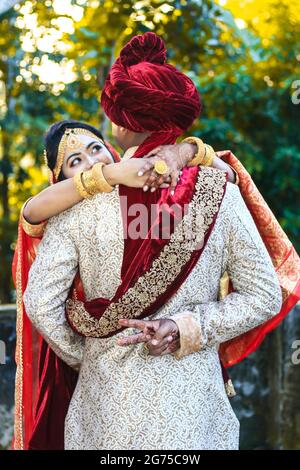Couple de mariage indien embrassant et marié montrant le signe de victoire avec fond vert bokeh. Banque D'Images