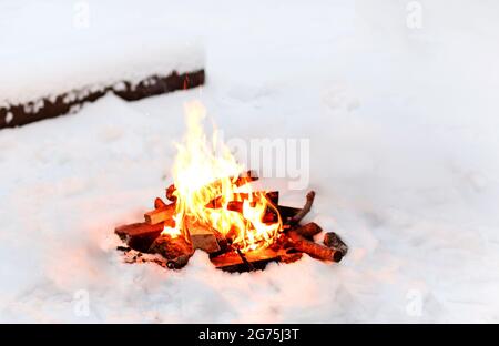 Feu de joie brillant brûlant sur un sol enneigé près des rondins en hiver soir dans les bois Banque D'Images