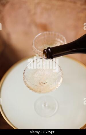 Par le dessus, une personne méconnaissable verse du champagne de la bouteille dans des gobelets en verre sur une table ronde Banque D'Images