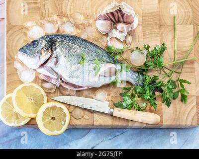 Poisson frais Dorado. La dorade crue au persil, à l'oignon, à l'ail et aux tranches de citron, recouverte de glace prête à cuire sur une planche de bois. Vue de dessus. Rétrogro en marbre Banque D'Images