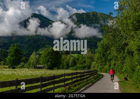 Chemin avec femme vêtue de rouge sur le vélo près de la clôture en bois et de couleur fraîche prairie Banque D'Images