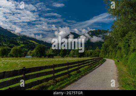 Chemin avec femme vêtue de rouge sur le vélo près de la clôture en bois et de couleur fraîche prairie Banque D'Images