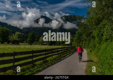 Chemin avec femme vêtue de rouge sur le vélo près de la clôture en bois et de couleur fraîche prairie Banque D'Images