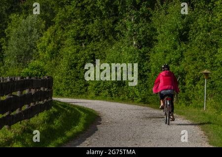 Chemin avec femme vêtue de rouge sur le vélo près de la clôture en bois et de couleur fraîche prairie Banque D'Images