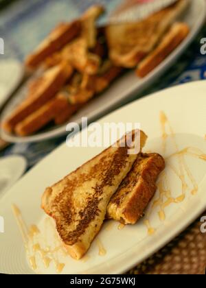 Deux toasts français servis avec du miel sur une assiette blanche pour le petit-déjeuner ou le brunch, en arrière-plan une pile de toasts français. Banque D'Images